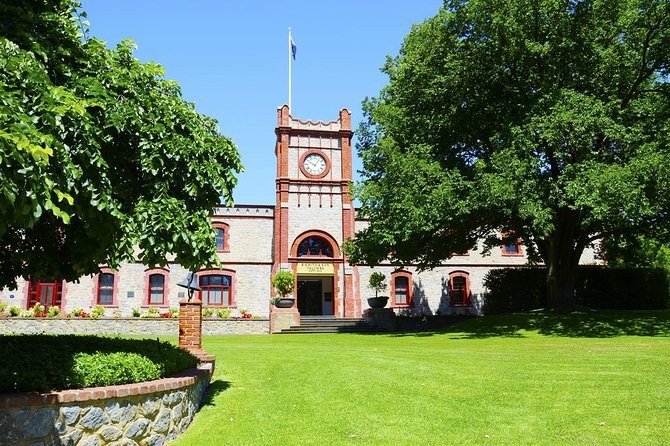 A stone winery with a red-brick clock tower, a flag and a mown lawn under old trees